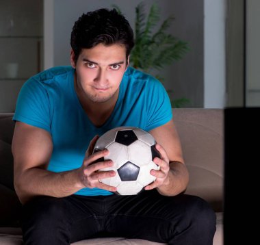 Genç adam gece geç saatlerde futbol seyrediyor.