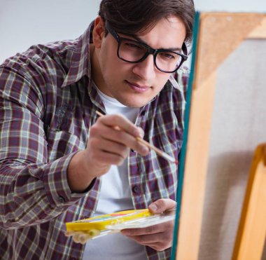 Genç erkek sanatçı parlak stüdyoda resimler çiziyor.