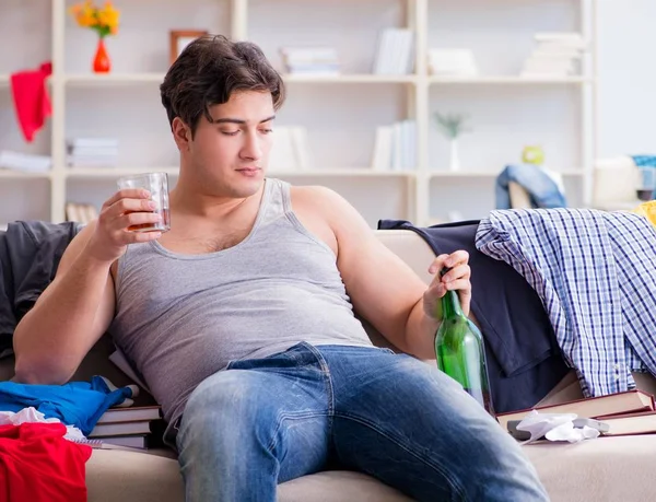 Jovem estudante bêbado beber álcool em um quarto bagunçado — Fotografia de Stock
