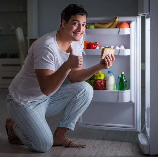 Человек в холодильнике ест ночью — стоковое фото