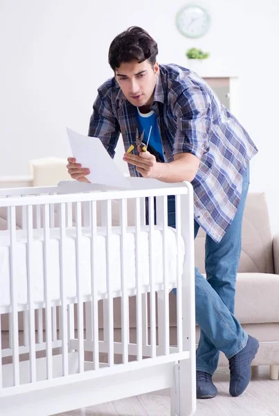 Νεαρός άνδρας συναρμολόγηση κρεβατιού μωρού με εγχειρίδιο οδηγιών — Φωτογραφία Αρχείου