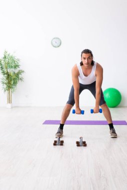 Genç yakışıklı adam içeride spor yapıyor.