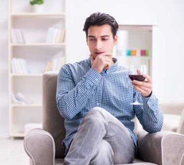 Genç adam evde şarap içiyor.