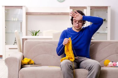 Genç yakışıklı adam evde örgü örüyor.