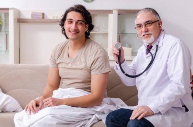 Yaşlı erkek doktor genç erkek hastayı ziyaret ediyor.