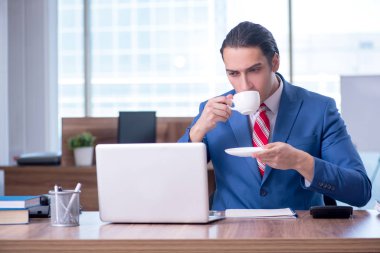 Genç yakışıklı işadamı ofiste oturuyor.