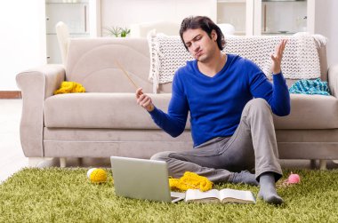 Genç yakışıklı adam evde örgü örüyor.