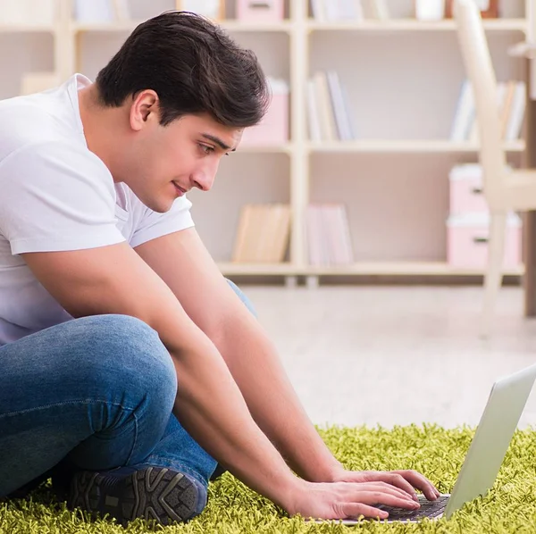 Чоловік працює на ноутбуці вдома на підлозі килима — стокове фото