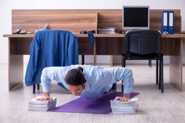 Genç yakışıklı işadamı iş yerinde egzersiz yapıyor.