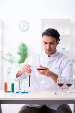 Erkek kimyager laboratuvarda şarap örneklerini inceliyor.