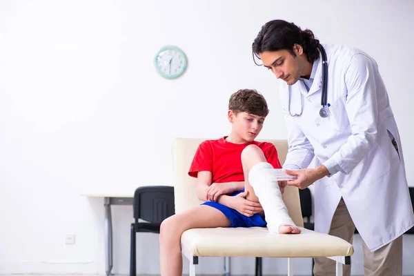 Perna ferido menino visitando jovem médico traumatologista — Fotografia de Stock
