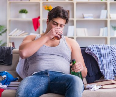 Dağınık bir odada alkol alan genç bir öğrenci.