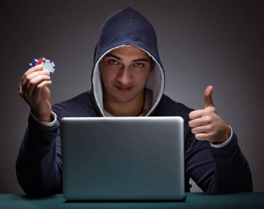 Kapüşonlu genç adam dizüstü bilgisayarın önünde oturuyor.