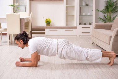 Genç adam evde fiziksel egzersiz yapıyor.