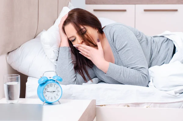 Mujer joven acostada en la cama en concepto de gestión del tiempo —  Fotos de Stock