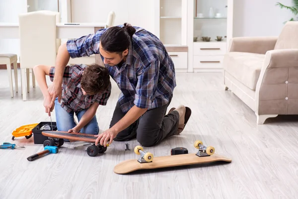 Νεαρός πατέρας επισκευή skateboard με το γιο του στο σπίτι — Φωτογραφία Αρχείου