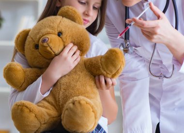 Kadın doktor oyuncak ayıyla küçük tatlı kızı muayene ediyor.