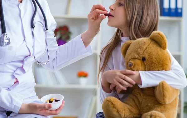 Donna medico femminile esaminando piccola ragazza carina con orso giocattolo — Foto Stock