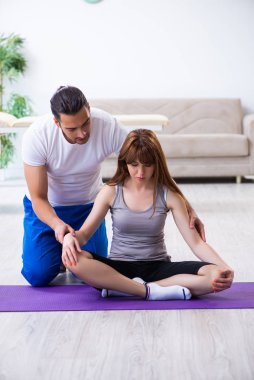 Erkek fizyoterapist yerde yaralı bir kadınla egzersiz yapıyor.