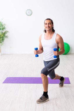 Genç yakışıklı adam içeride spor yapıyor.