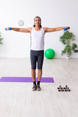 Genç yakışıklı adam içeride spor yapıyor.