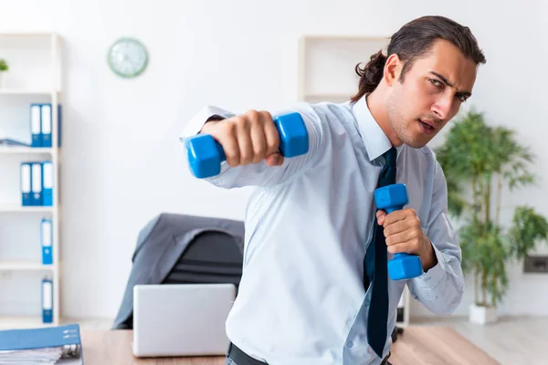 Jovem e bonito funcionário fazendo exercícios esportivos no local de trabalho — Fotografia de Stock