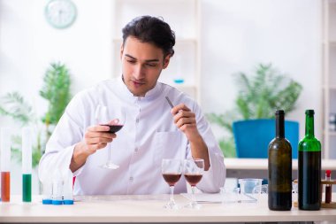Erkek kimyager laboratuvarda şarap örneklerini inceliyor.