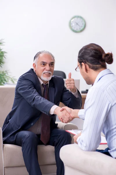 Oude man op bezoek bij jonge mannelijke dokter psycholoog — Stockfoto