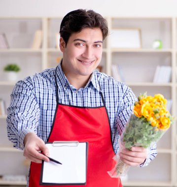 Çiçekçi yardımcısı bir demet çiçek sunuyor.
