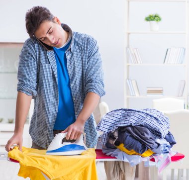 Genç adam evde çamaşır ütülüyor.