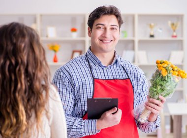 Çiçekçi yardımcısı kadın müşteriye çiçek satıyor.