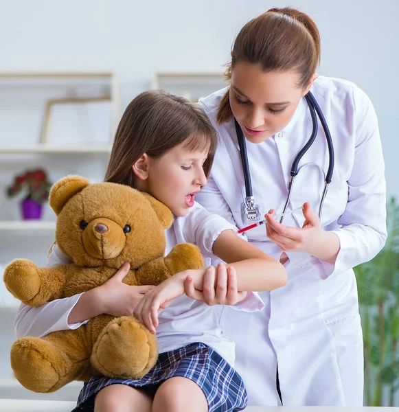 A mulher médica examinando pequena menina bonito com urso de brinquedo — Fotografia de Stock