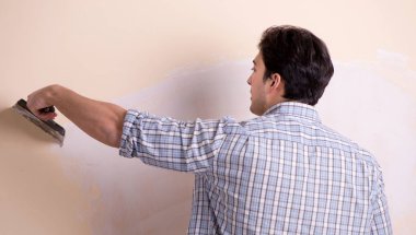 Evdeki duvara alçı yapıştıran genç adam.