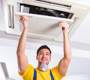 Tamirci tavan havalandırma ünitesini tamir ediyor.