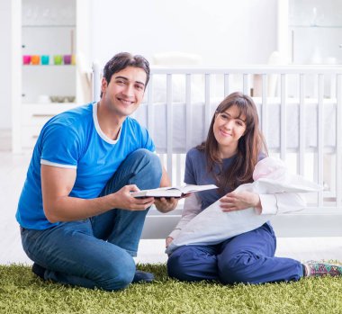 Yeni doğmuş bebekleriyle halıda oturan genç ebeveynler.