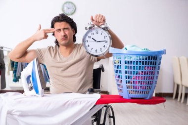 Tekerlekli sandalyedeki genç adam evde ütü yapıyor.