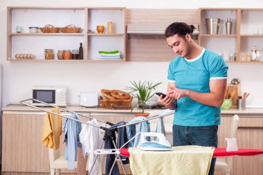 Genç adam evde çamaşır ütülüyor.