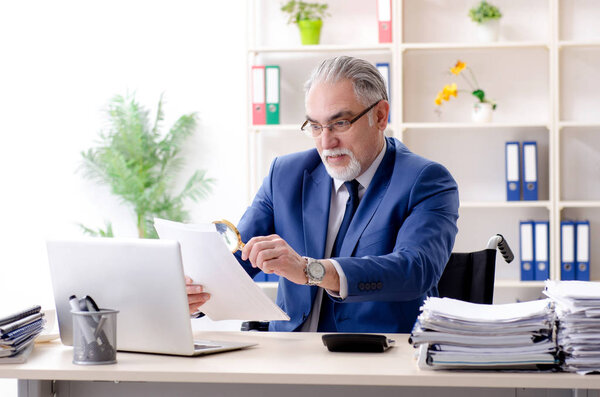 Пожилой работник в инвалидной коляске работает в офисе
