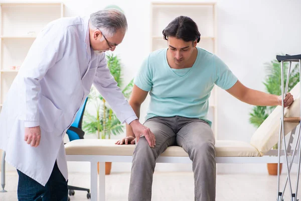 Joven pierna lesionada paciente masculino visitando viejo médico — Foto de Stock