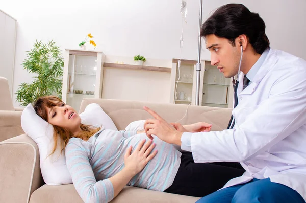 Молодой красивый врач навещает беременную женщину дома — стоковое фото