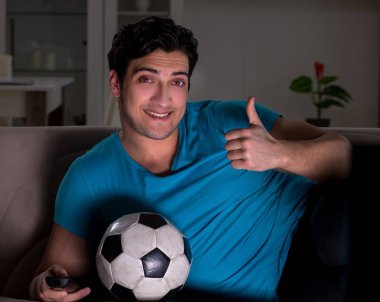 Genç adam gece geç saatlerde futbol seyrediyor.