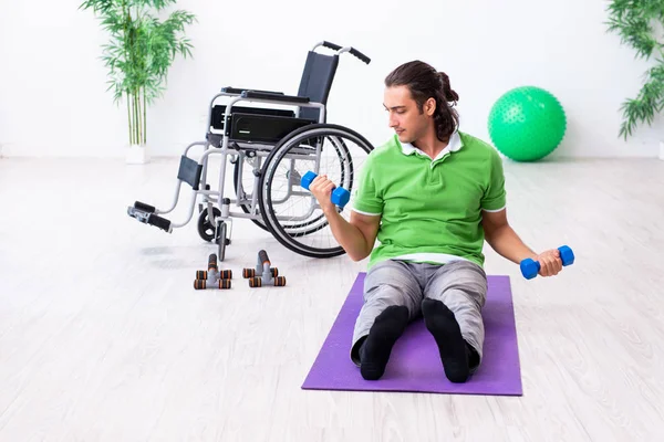 Молодой человек в инвалидной коляске делает упражнения в помещении — стоковое фото