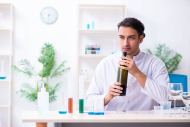 Erkek kimyager laboratuvarda şarap örneklerini inceliyor.