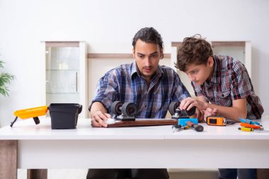 Genç baba oğluyla kaykay tamir ediyor.