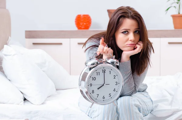 Mujer joven acostada en la cama en concepto de gestión del tiempo —  Fotos de Stock