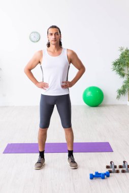 Genç yakışıklı adam içeride spor yapıyor.