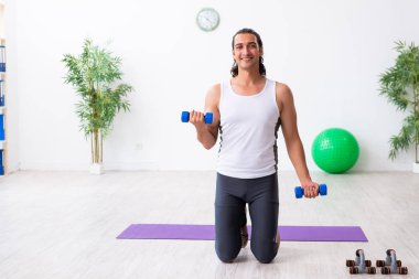 Genç yakışıklı adam içeride spor yapıyor.