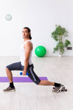Genç yakışıklı adam içeride spor yapıyor.