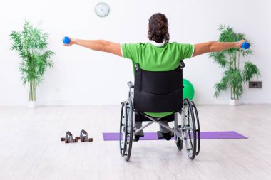 Tekerlekli sandalyedeki genç adam içeride egzersiz yapıyor.