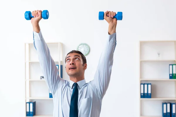 Jovem e bonito funcionário fazendo exercícios esportivos no local de trabalho — Fotografia de Stock